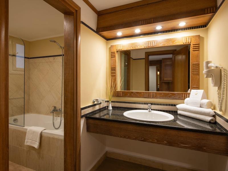 Koupelna s umyvadlem, zrcadlem s dřevěným rámem a vanou s ručníkem uvnitř.