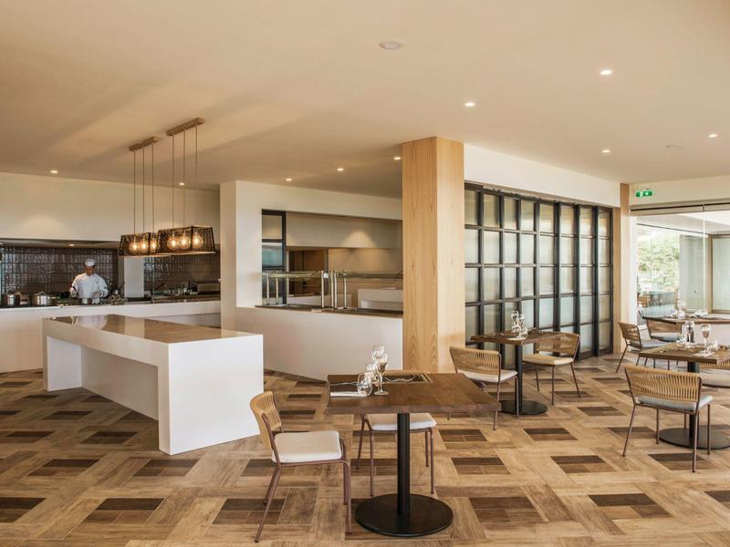 Moderní hotelová odpočinková zóna s stoly, židlemi a teplým barevným kobercem.