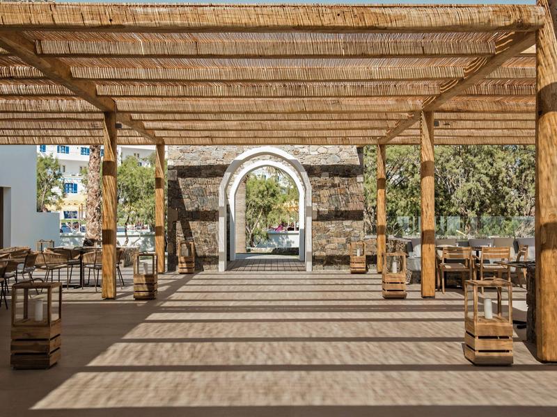 Krytá venkovní lounge s dřevěnými trámy, posezením a výhledem na kamenný oblouk.