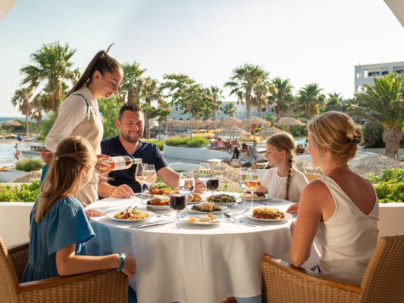 Rodina si užívá jídlo s výhledem na bazén a palmy v hotelové restauraci.