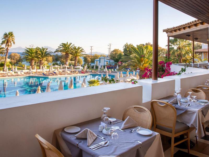 Stůl s příbory vedle terasy s výhledem na bazén a palmy v slunném hotelu