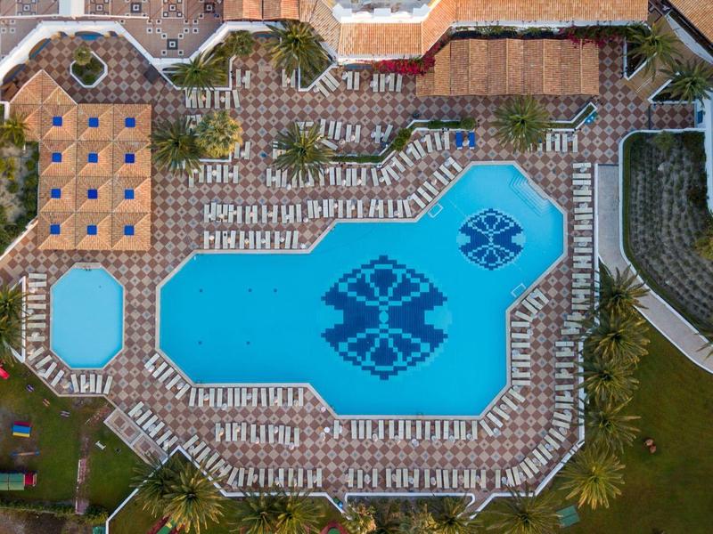 Letecký pohled na velkou oblast bazénu s mnoha lehátky a stinnými místy v rezortu.