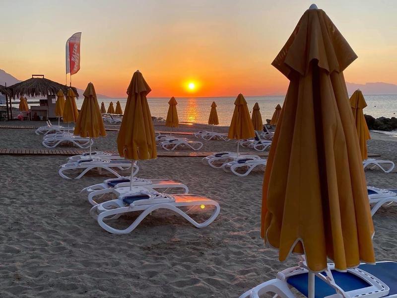 Západ slunce na pláži s lehátky a zavřenými slunečníky na písku.