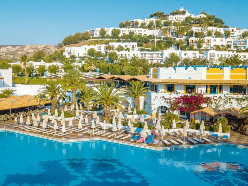 Velký venkovní bazén před bílým hotelovým komplexem pod jasnou modrou oblohou.