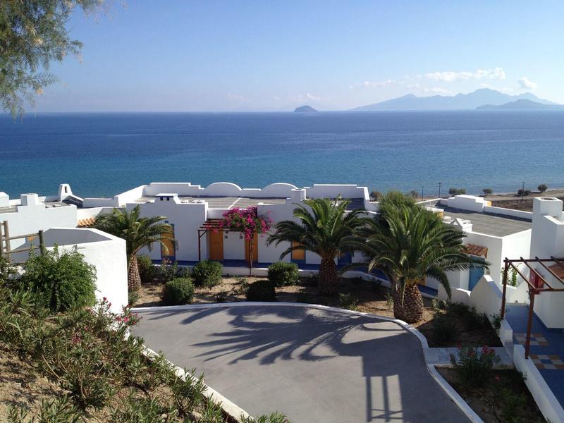 Pohled na bílé budovy a palmy podél pobřeží s modrým mořem a jasnou oblohou.