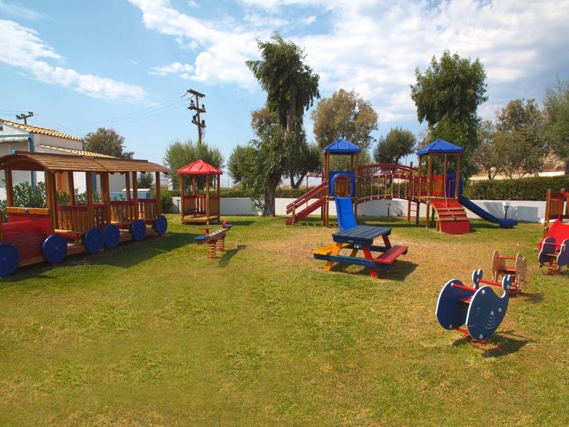 Barevné dětské hřiště se skluzavkami a zařízeními na trávníku pod modrou oblohou.