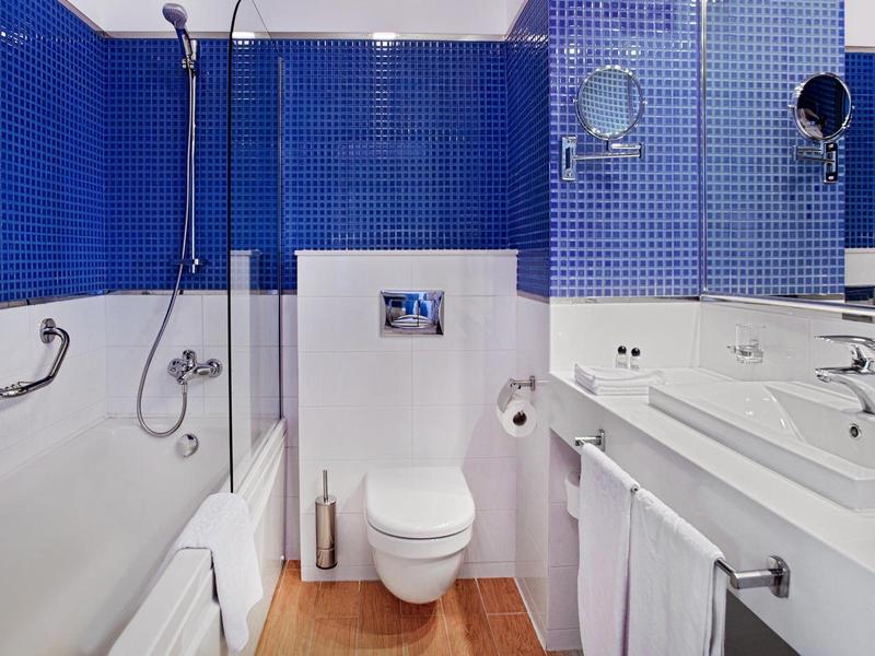 Moderní koupelna s modrými dlaždicemi, toaletou, umyvadlem a ručníky.