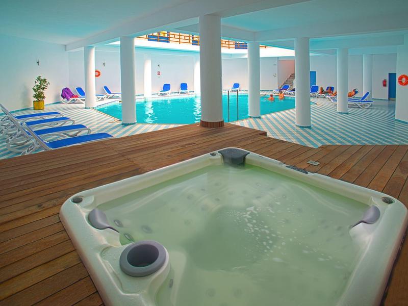 Vnitřní prostor hotelu s vířivkou v popředí a bazénem v pozadí.