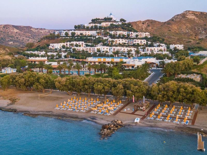 Luxusní plážový hotel s lehátky, bazénem a kopci v pozadí.