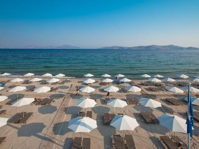 Strand mit vielen weißen Sonnenschirmen und Liegestühlen am ruhigen Meer an einem klaren Tag.