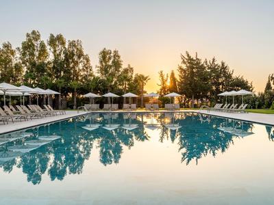 Ein ruhiger Pool bei Sonnenuntergang, umgeben von Liegestühlen und Bäumen.