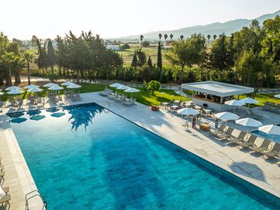 Großer Hotelpool mit Liegestühlen und Sonnenschirmen umgeben von Bäumen und Hügeln.