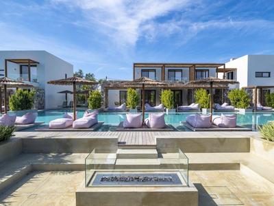 Moderner Hotelpoolbereich mit Sonnenliegen, Grünpflanzen und zweistöckigen Gebäuden im Hintergrund.