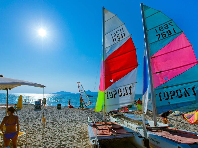 Zonnig strand met kleurrijke zeilboten en mensen die genieten van de heldere, blauwe zee.