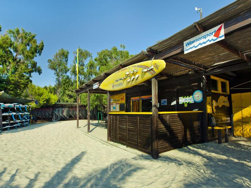 Buitenstrandbar met geel surfplankbord en zandgrond onder een heldere blauwe lucht.