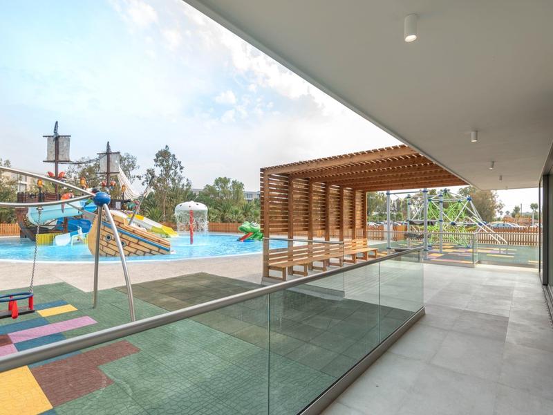 Moderne terras met uitzicht op een kleurrijke speeltuin en waterpark onder een blauwe lucht.