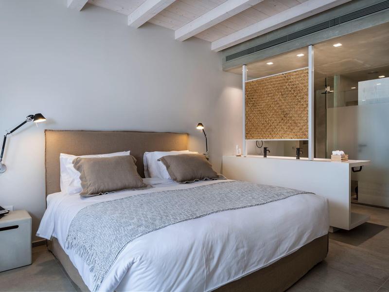 Moderne slaapkamer met groot bed, neutrale tinten en open badkamer gescheiden door glas.