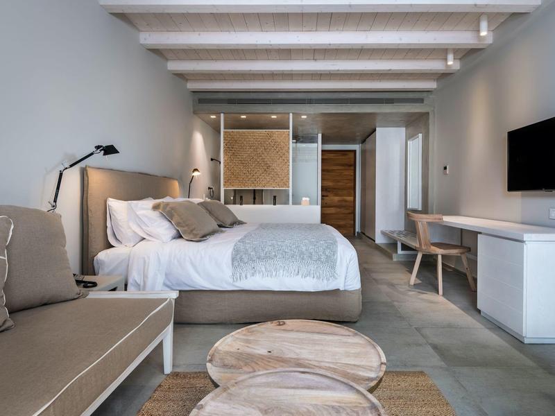 Moderne hotelkamer met bed, bank, houten tafels en een aan de muur bevestigde tv.