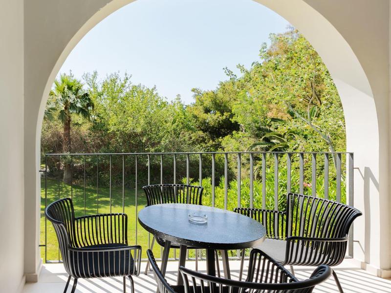 Buitenpatio met zwarte stoelen en tafel onder een witte boogplafond met uitzicht op een groen tuin.