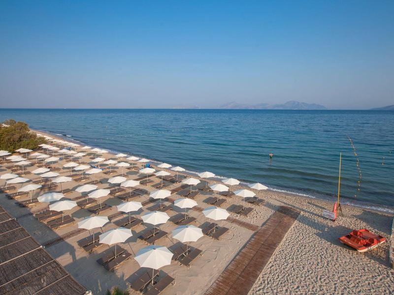 Strand met veel witte parasols langs heldere zee onder een blauwe lucht.