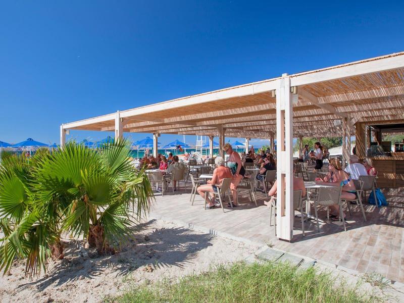 Strandrestaurant met mensen die eten onder een overdekt terras op een zonnige dag.