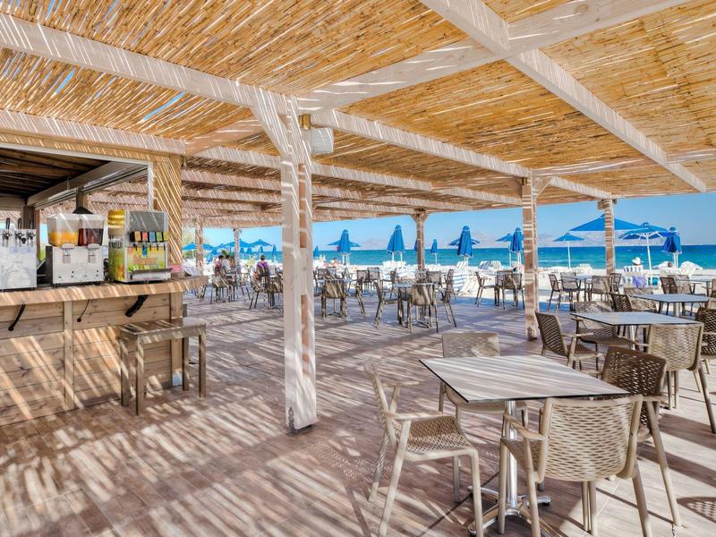 Buitenbar aan het strand met tafels, stoelen en parasols met uitzicht op de zee.