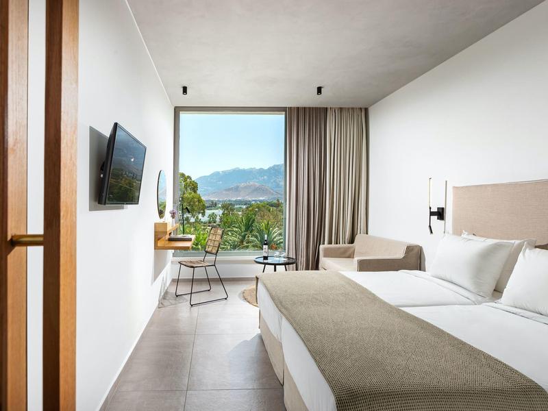 Lichte hotelkamer met groot bed, tv en balkon met uitzicht op de bergen.