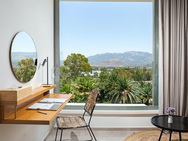 Moderne hotelkamer met groot raam met uitzicht op bergen en palmbomen.