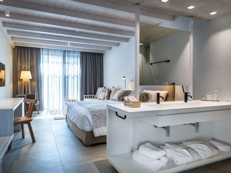 Moderne hotelkamer met kingsize bed, zacht licht, bureau en badkamergedeelte gescheiden door een halve muur.