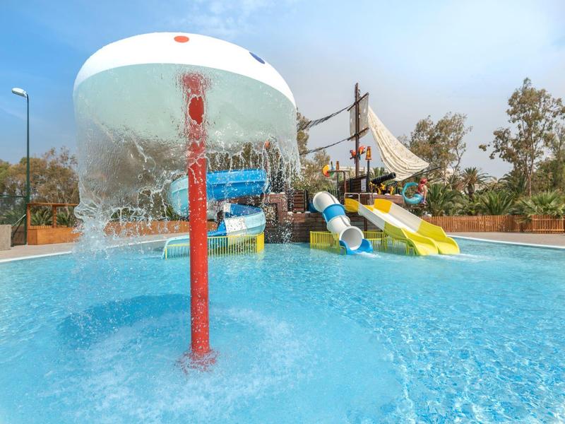 Buitenspeelruimte met waterrugzak en kleurrijke glijbanen onder een heldere lucht.