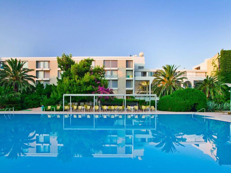 Zwembad met helder blauw water voor een modern laag hotel omgeven door palmbomen.