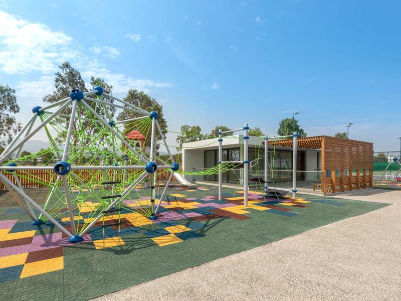 Moderne buitenspeelweide met klimstructuur en glijbanen nabij een gebouw onder blauwe lucht.