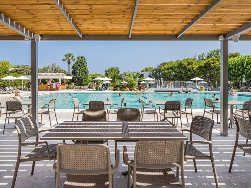 Buitendining met tafels en stoelen bij een zwembad onder een houten pergola