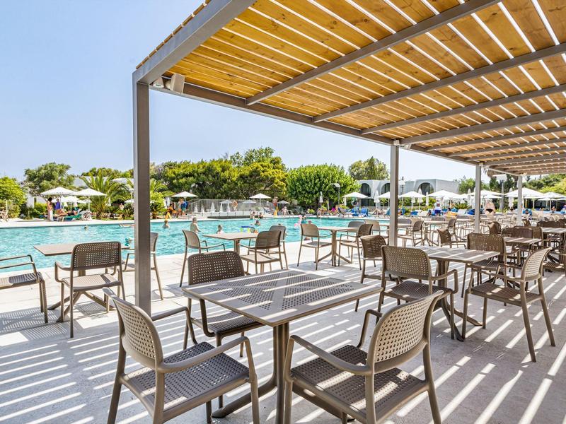Buiten zitgedeelte met tafels en stoelen onder een pergola bij een groot hotelzwembad.