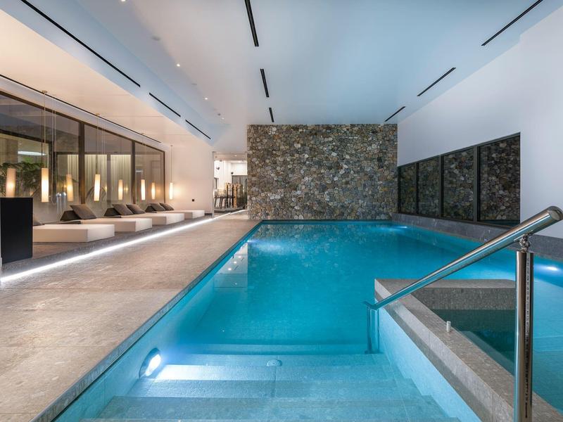 Binnenzwembad met blauw water, stenen muur en sfeerverlichting in een modern hotel.