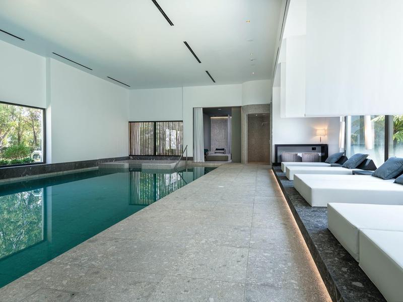 Binnenzwembad met ligstoelen en grote ramen die natuurlijk licht binnenlaten