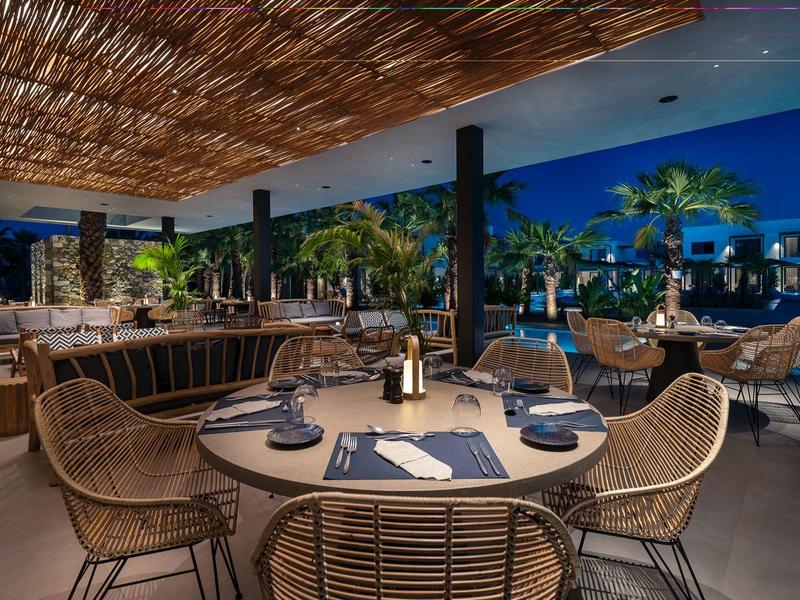 Buiten zitgedeelte van restaurant met ronde tafel en rieten stoelen onder een overkapping.