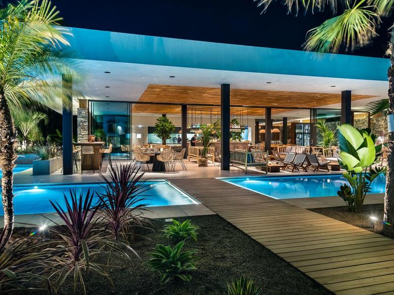 Moderne hotel buitenterrein met zwembaden en houten pad 's nachts.