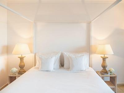 Cozy double bed with four white pillows flanked by nightstands and lamps.