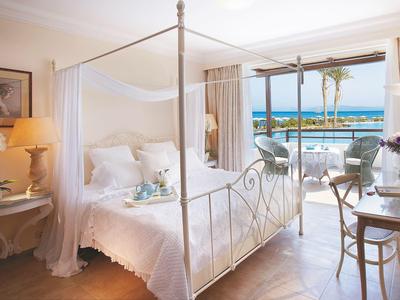 Bright hotel room with canopy bed, sea view balcony, and cozy decor.