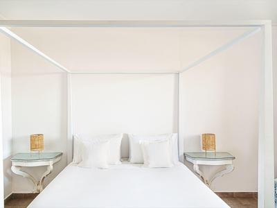 Brightly lit bedroom with white canopy bed and bedside tables with lamps.