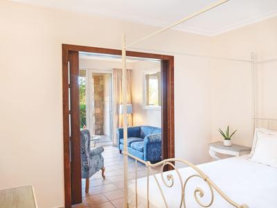 Bright hotel room with white bed, small side table, and view into a living room with blue couch.