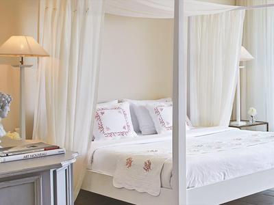 Bright bedroom with white canopy bed, sheer curtains, and lamp beside the bed.
