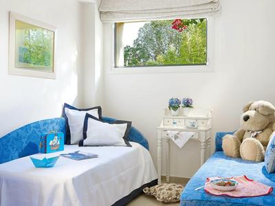 Bright hotel room with blue sofa bed, white linens, side table, and a large teddy bear.