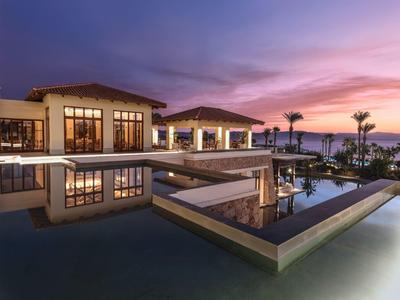 Modern hotel pool at sunset with reflective water and palm trees.