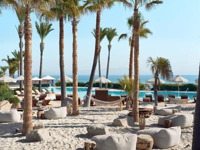 Strandresort mit Palmen, Sitzsäcken und Sonnenschirmen am Meer bei klarem Himmel.