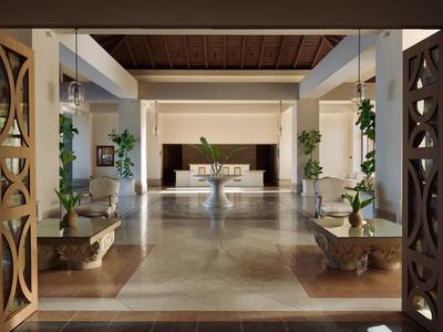 Spacious hotel lobby with marble flooring, modern furniture, and plants in containers.