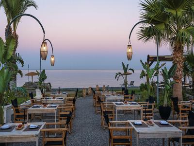 Seaside restaurant terrace with wooden tables and chairs at sunset.