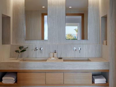 Moderner Hotelbadezimmerbereich mit Doppelwaschbecken, zwei Spiegeln und Holzregalen mit Handtüchern.