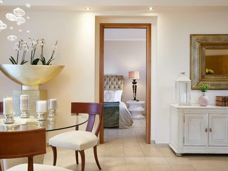 Elegant hotel room entrance with wooden chairs, white sideboard, and decorative plants and candles.
